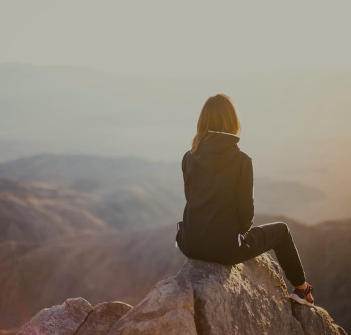 Person, die tagsüber auf einem grauen Felsen mit Blick auf den Berg sitzt